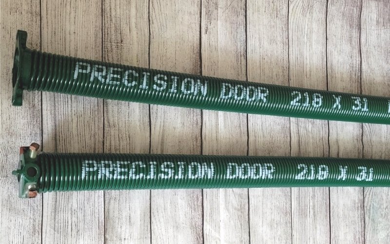 Lengthwise photo of a green garage door spring that says "Precision Garage Door"